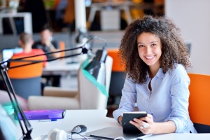 women sitting at her desk smiling on her tablet