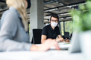 young people who are retain employees with face masks back at work in office after lockdown