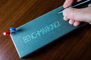 man writing benchmarking on grey paper